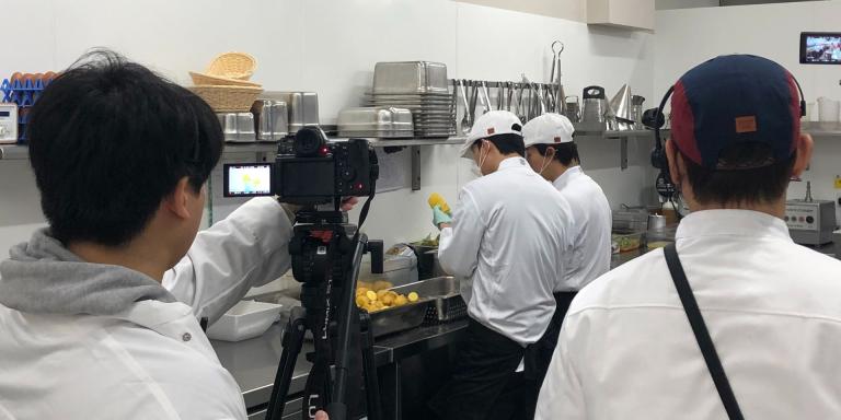 A film crew dressed in chefs whites shooting a TV show in a commercial kitchen