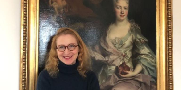 Pauline Baer de Perignon, who has long dark blonde hair and is wearing a black turtleneck sweater, stands in front of a portrait painting