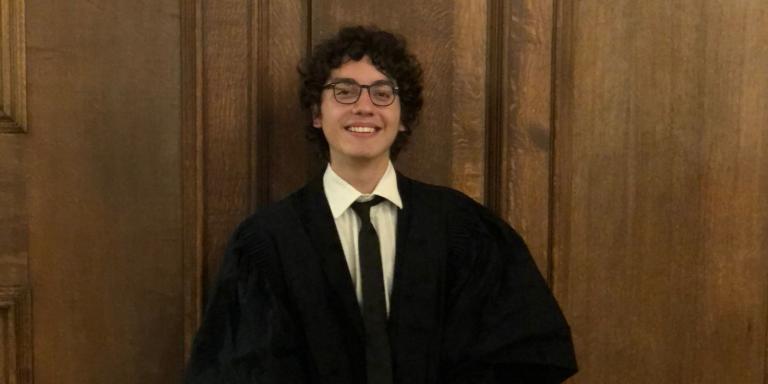 Photo of Cem Kozanoglu, who has short dark curly hair and is wearing a black Oxford academic gown
