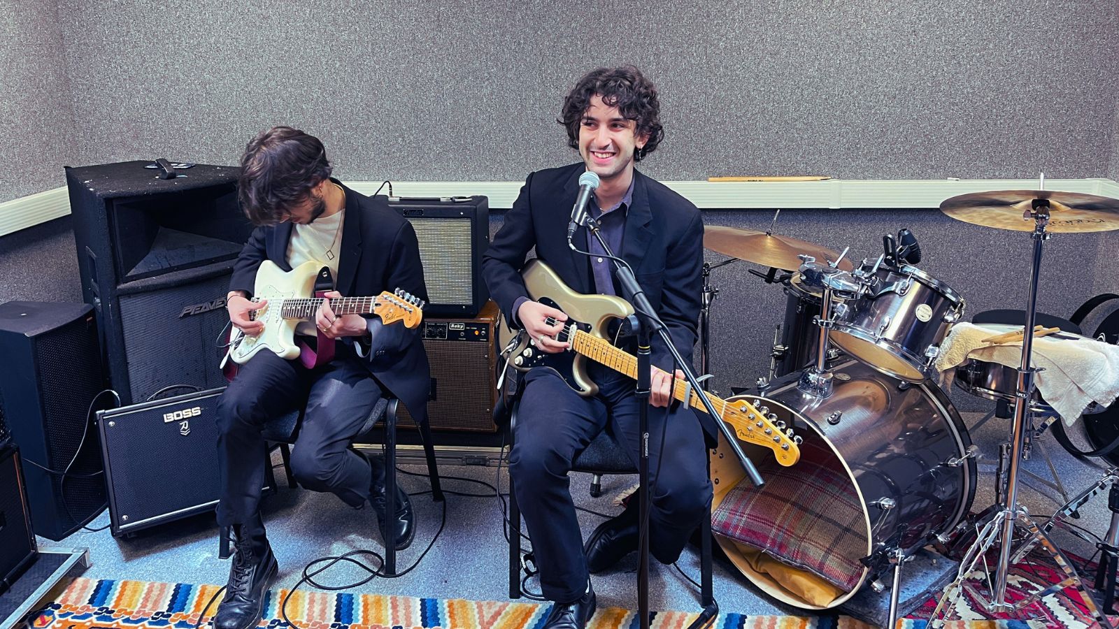 Photo of two young men with guitars sitting in a music studio space about to perform