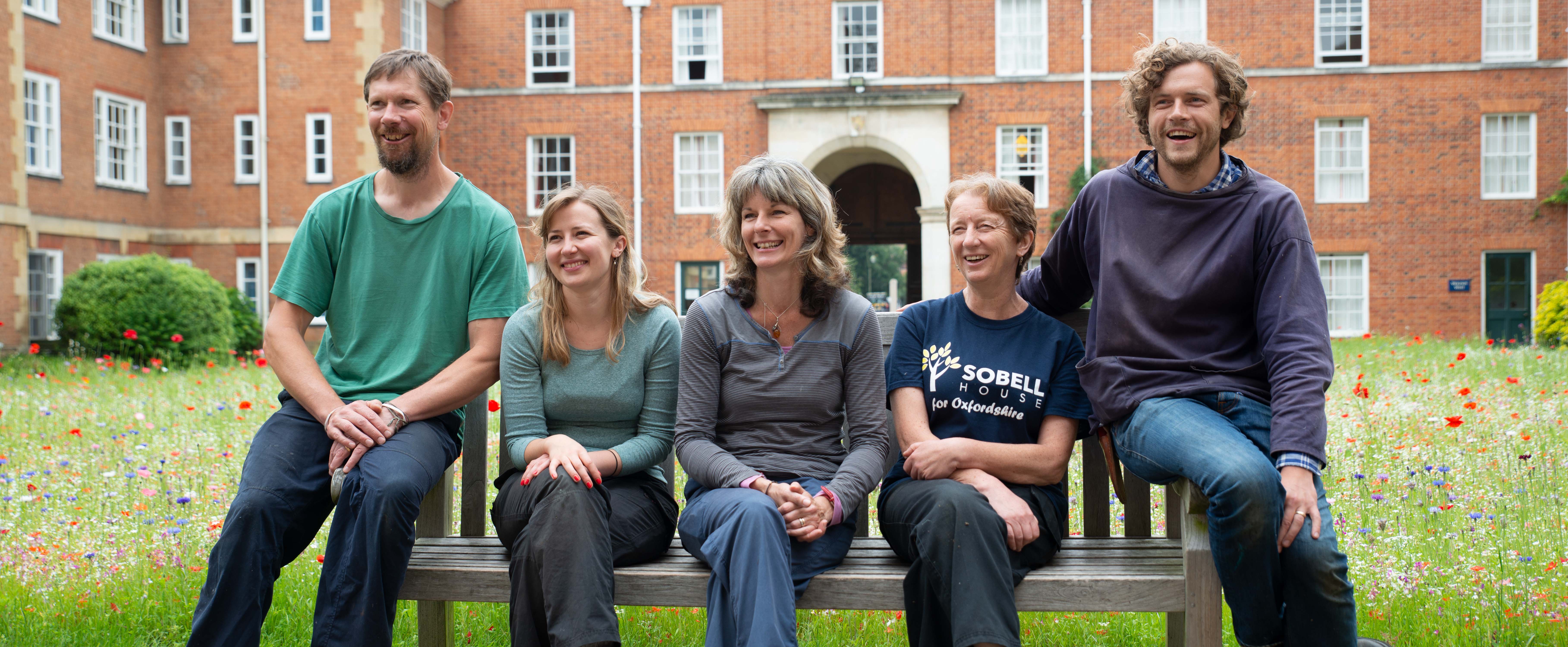 LMH Gardening Team sitting on bench in front of wild flower meadow in the quad