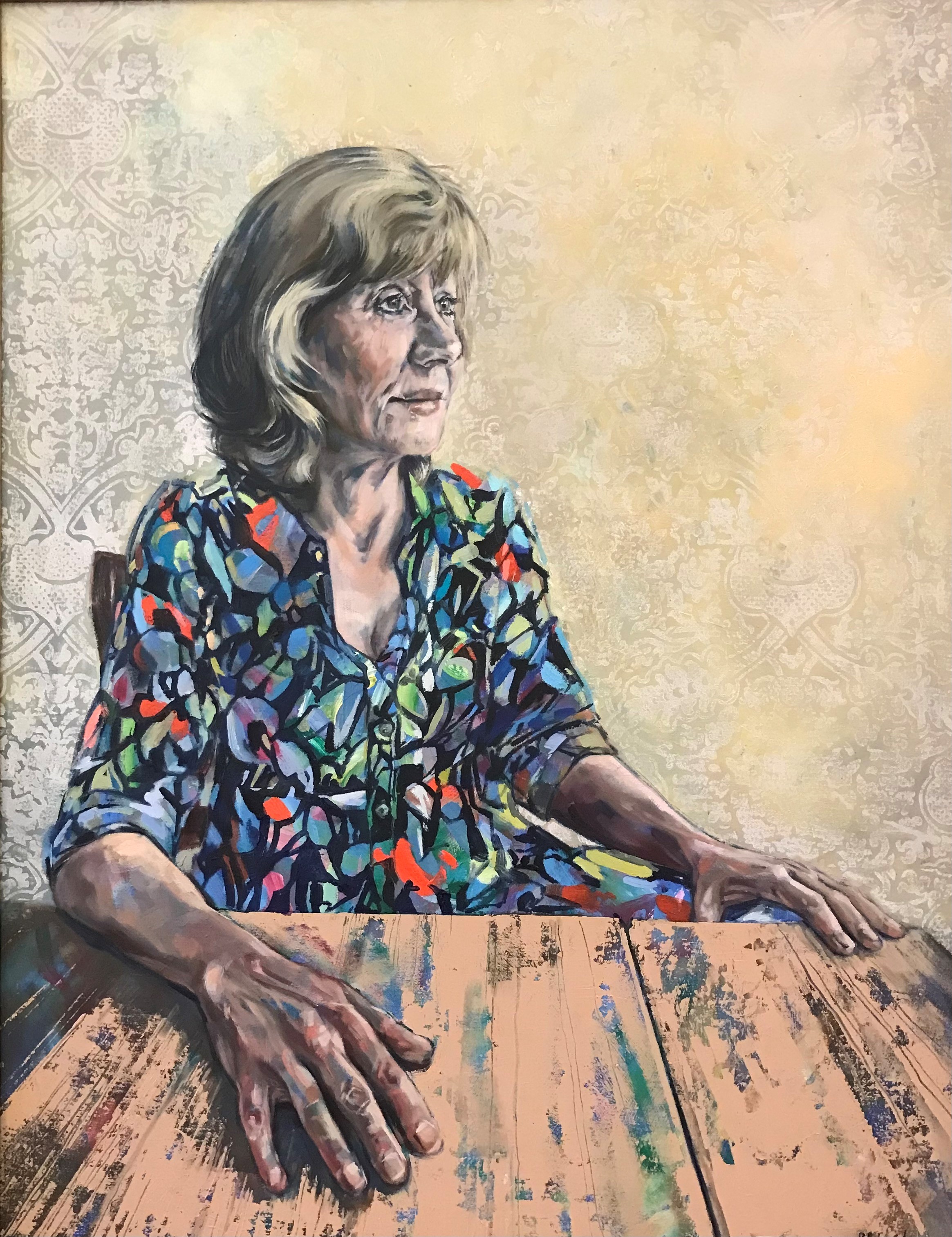 A portrait of a woman wearing a brightly coloured dress sitting at a wooden table