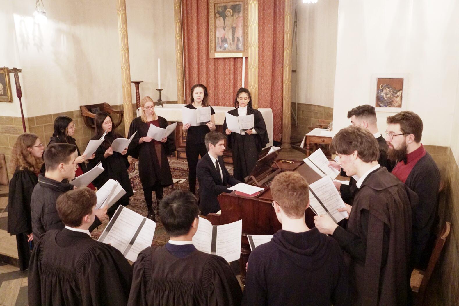 The LMH Choir singing in a circle which surrounds the LMH Director of Chapel Music playing the piano inside the LMH Chapel.
