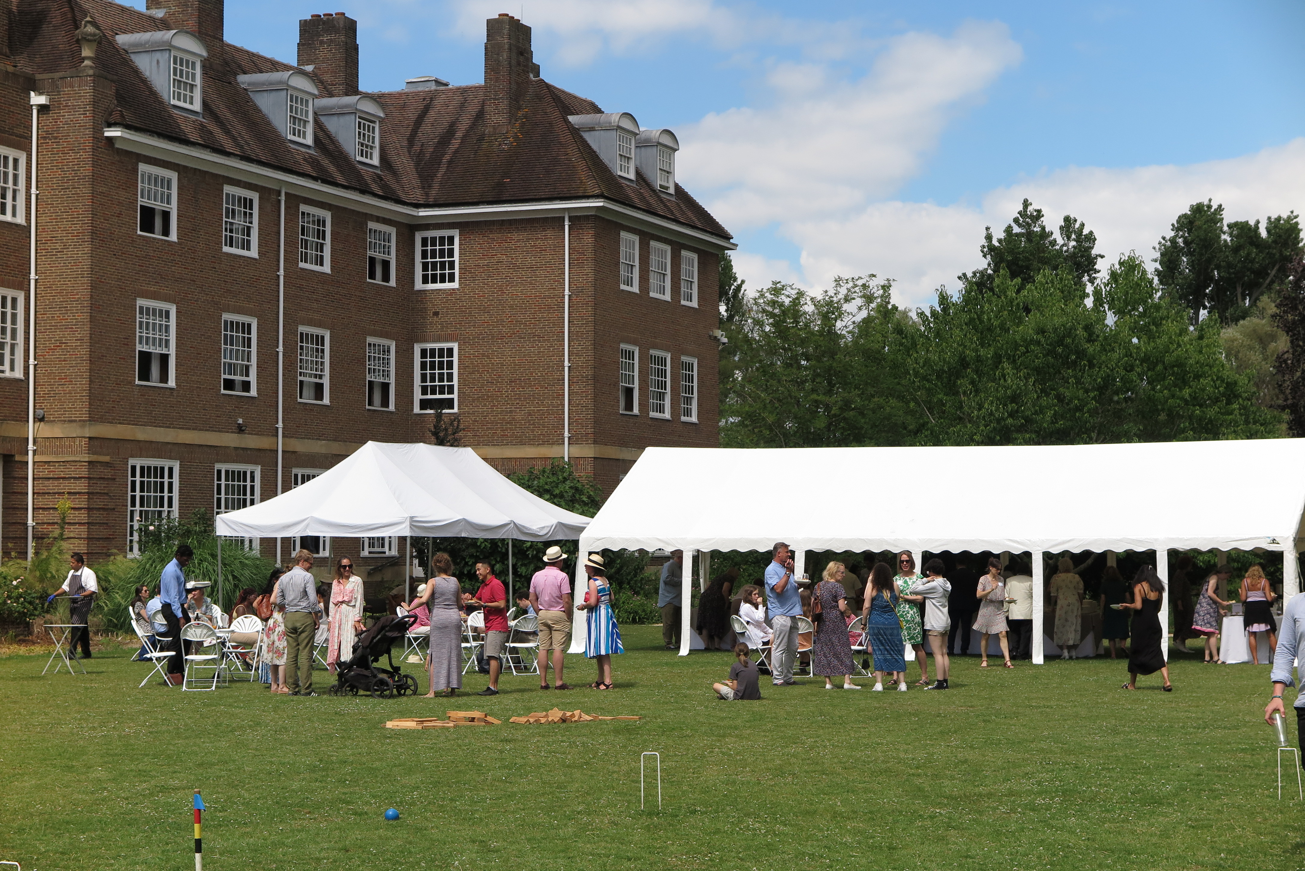 Photo of people gathered around a large white marquee on a green lawn at a garden party
