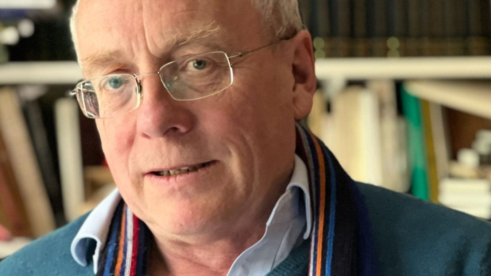 Close-up photo of a man wearing glasses standing in front of a bookshelf