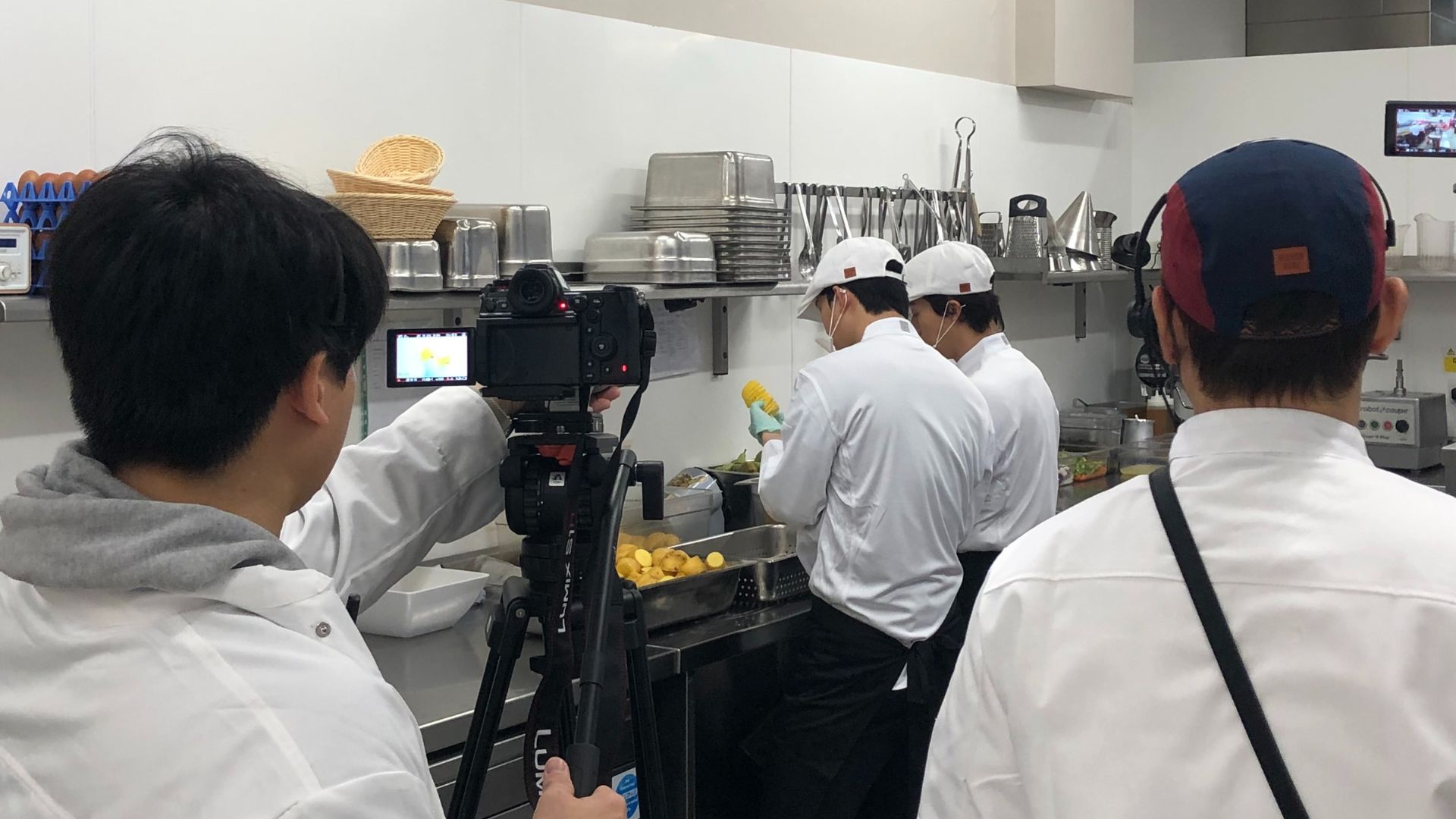 A film crew dressed in chefs whites shooting a TV show in a commercial kitchen