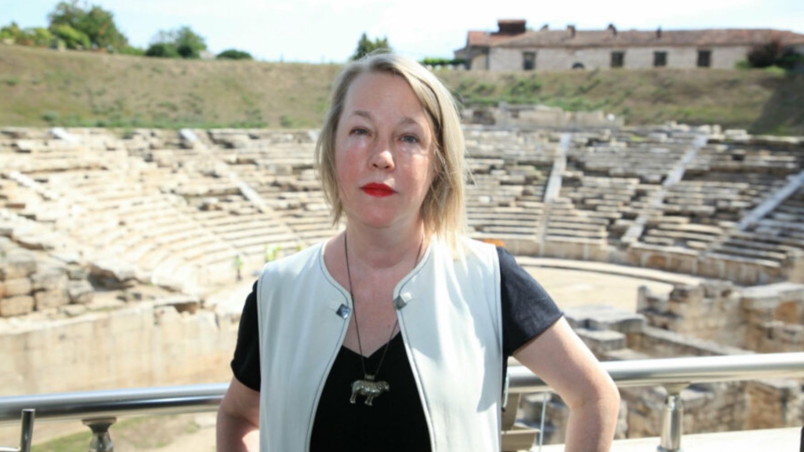 A.E. Stallings, a woman with short blonde hair, stands in front of a greek ampitheatre
