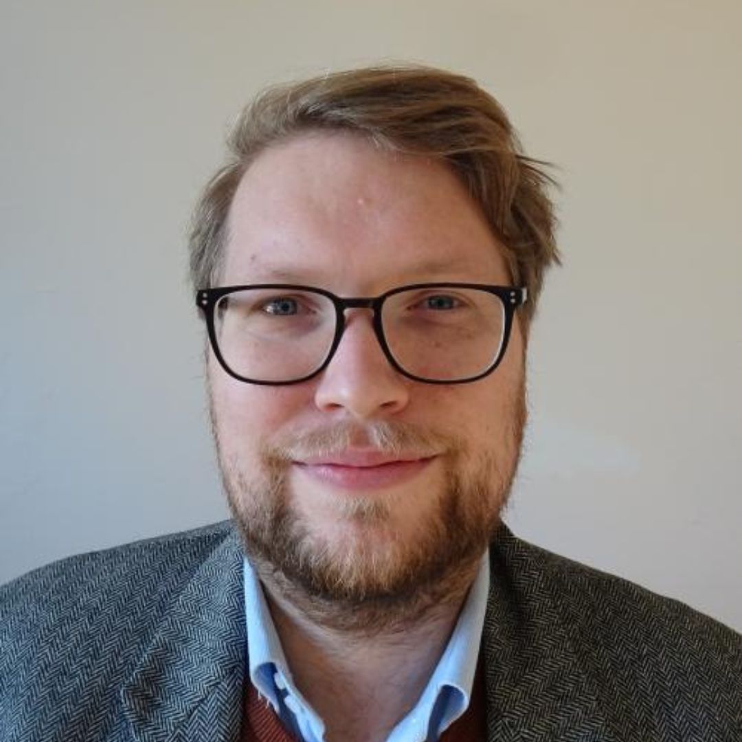 A man with short brown hair and dark rimmed glasses