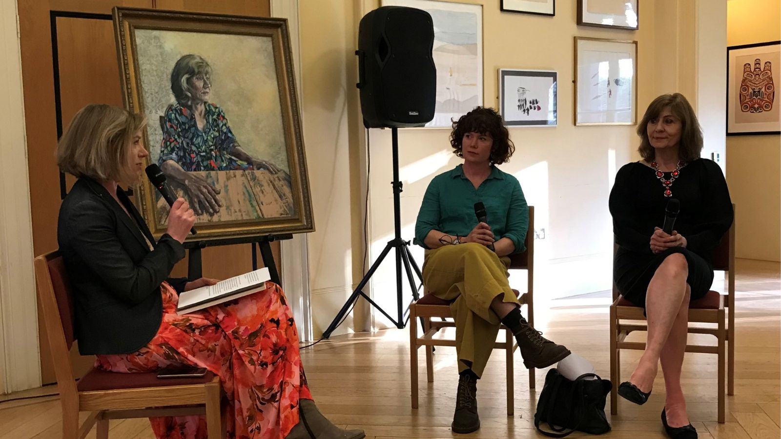 Three women sit in front of a portrait of Professor Christine Gerrard