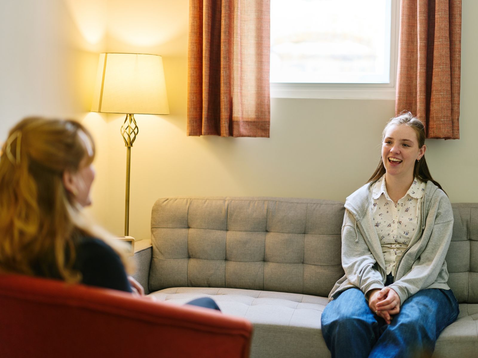 A student sits on a pale grey sofa in conversation with a woman