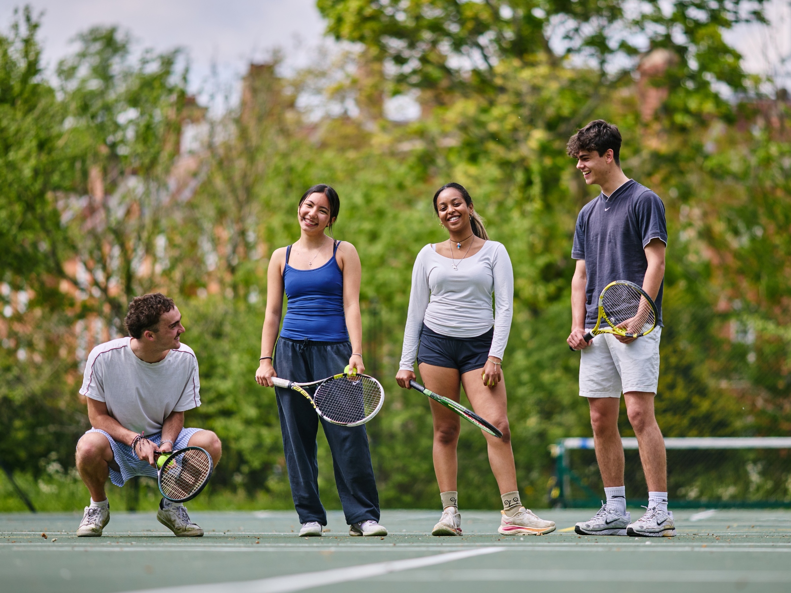 Four young people on a tennis court holding racquets