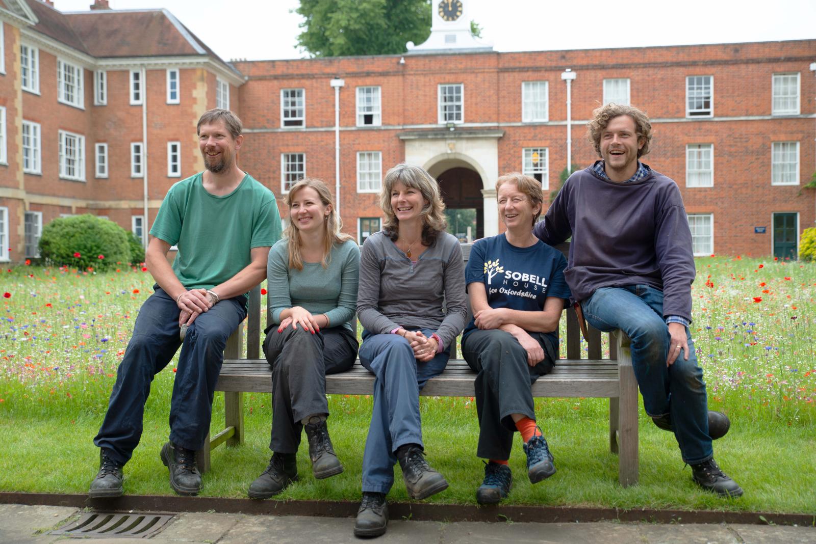 LMH Gardening Team sitting on bench in front of wild flower meadow in the quad