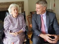 Elizabeth Kaser, who has short white hair and sits in a wheelchair, sits next to Professor Stephen Blyth, who wears a grey suit