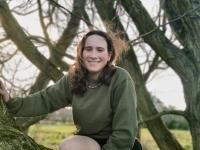 A woman with long dark hair sitting in a tree smiling.