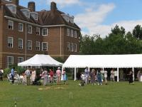 Photo of people gathered around a large white marquee on a green lawn at a garden party