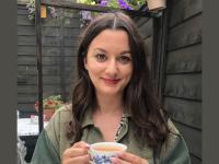A woman with long dark brown hair sitting in a garden with a cup of tea