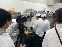 A film crew dressed in chefs whites shooting a TV show in a commercial kitchen