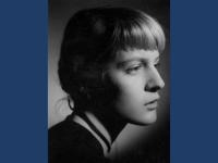A black and white portrait photo of a young woman with tied-back blonde hair and a fringe