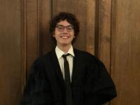 Photo of Cem Kozanoglu, who has short dark curly hair and is wearing a black Oxford academic gown