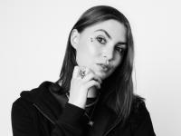 Black and white photo of Emmeline Armitage, a woman in her mid-twenties with long dark brown hair. She is looking at the cameral with her eyebrow raised.
