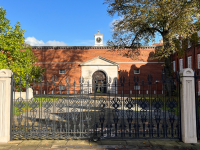 A beautiful image of the front of Lady Margaret Hall, with a set of wrought iron gates in front of an imposing red brick building set against a bright blue sky