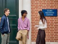 Two male and one female student lean against a red brick building, the Clore Graduate Centre