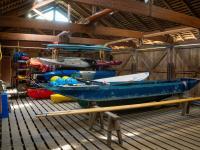 The interior of a wooden boathouse, with kayaks stacked neatly on racks