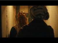A still from Onyeka Igwe's film 'A Radical Duet', showing two women wearing headscarves facing away from the camera and walking down a dimly lit corridor