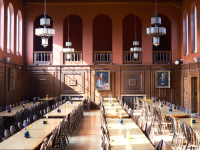 A view of the inside of the LMH dining hall, which has deep pinky red walls, wooden panelling and light streaming through the high windows