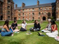 Students sitting on the grass outside some tall red brick buildings