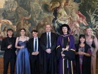 A group of LMH Tutors and students in formal clothes, celebrating while standing in front of a tapestry