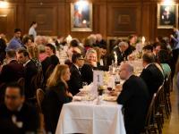Guests seated at candlelit tables during a formal dinner in a wood-panelled college hall.