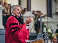 Professor Stephen Blyth in a red academic gown speaking in the Sheldonian