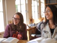 Two students smile while sitting at a desk with books open.