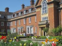 A red brick building with many windows, and in the foreground bright coloured tulips flower in a garden