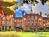 A large red brick building seen through a screen of autumn leaves