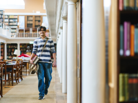 LMH student walking through the college library carrying books and a satchel