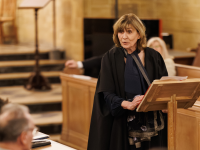 Professor Christine Gerrard, wearing black academic robes, speaks at a wooden lectern in the LMH Chapel, addressing an audience seated in wooden pews.