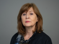 Portrait of Professor Christine Gerrard, wearing a dark sweater and patterned scarf, against a plain grey background