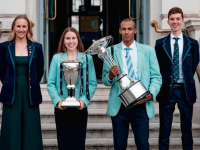 Two women and two men dressed in University of Oxford and University of Cambridge Blazers stand on some steps. One woman holds a large silver trophy