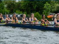 Women wearing blue and white lycra rowing suits sitting in a boat and rowing in Oxford's summer eights competition on the River