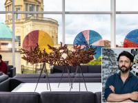Sculpture by Conrad Shawcross on display in Oxford’s Mathematical Institute, featuring a complex bronze geometric structure and colourful circular artworks in the background. An inset shows a portrait of Shawcross with arms folded, standing in front of another sculptural work.