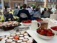 Guests strolling through the LMH gardens in bright summer sunshine during the 2025 Alumni Garden Party, with families and alumni gathered near the red-brick building.