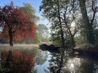 Boats on the River Cherwell at Lady Margaret Hall, Oxford, with morning mist rising and autumn trees reflected in the water.