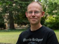 Peter Thonemann, who has very short brown hair, rimless glasses and is wearing a black t-shirt with 'Phoebe Bridgers' printed on it