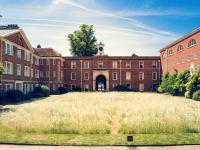 A view of LMH's Talbot Quad, looking across a wildflower meadow towards red brick buildings with a clock tower