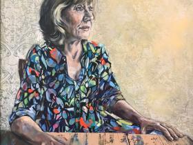 A portrait of a woman wearing a brightly coloured dress sitting at a wooden table