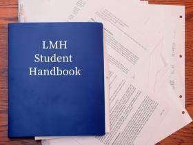 A blue book with papers spilling out of it with the words: LMH Student Handbook