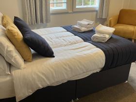 A double bed with a white beadspread, with towels laid out on top