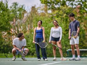 A group of four students standing on a blue hard-court tennis court in the LMH gardens